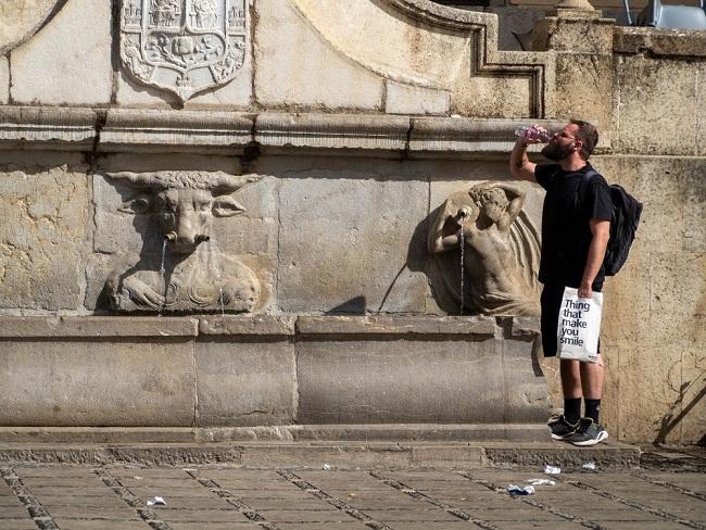 Un hombre bebe agua en una fuente junto a Plaza Nueva. 