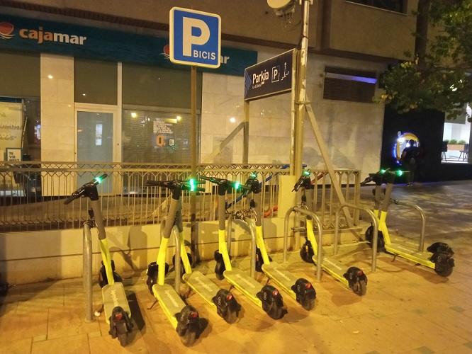 Patinetes eléctricos de alquiler en un aparcamiento para bicicletas.