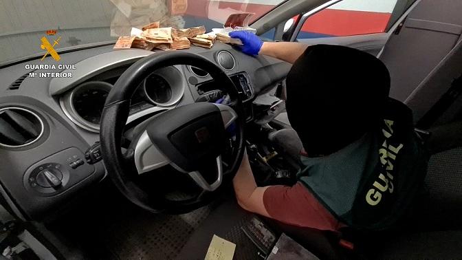 Un agente saca fajos de billetes escondidos en un vehículo. 