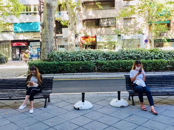 Dos jóvenes, con mascarillas, sentadas en bancos en la Carrera de la Virgen.