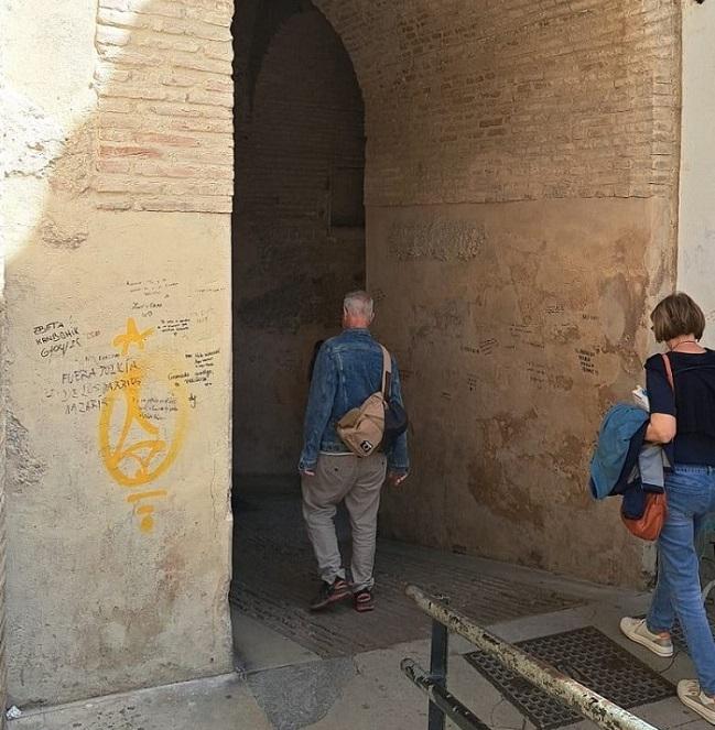 Turistas transitan por el Arco de las Pesas, lleno de pintadas. 
