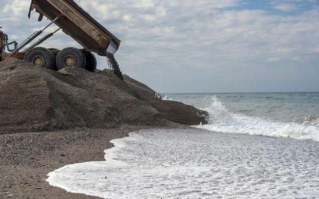 Un camión echa arena en Playa Granada mientras el agua se la lleva. 