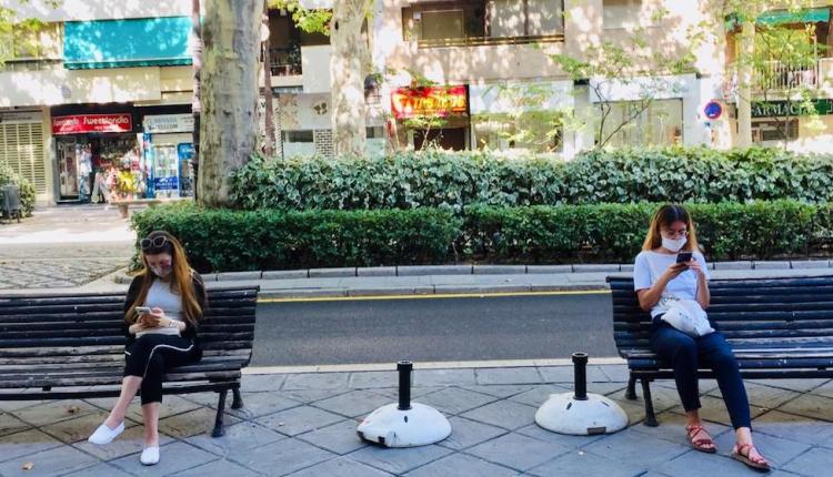 Dos jóvenes, sentadas con mascarilla, observan sus teléfonos móviles