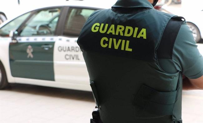 Un agente de la Guardia Civil, de espaldas, junto a un vehículo oficial. 