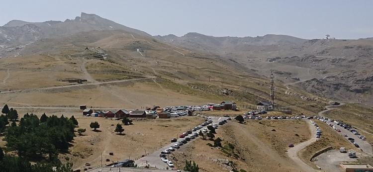 Zona de la Hoya de la Mora, llena de vehículos, con el Veleta al fondo a la izquierda. 