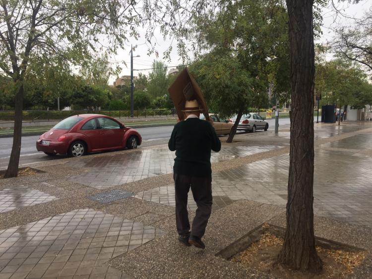 La lluvia le sorprende y debe guarecerse bajo un cartón.