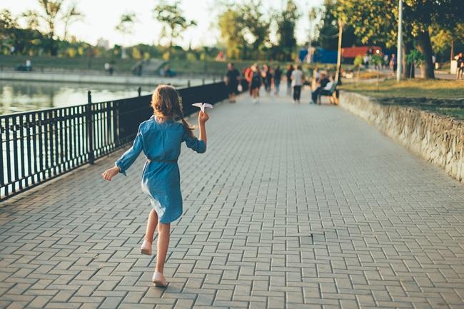 Una niña juega en la calle con un avión de papel.