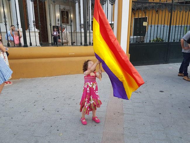 Una pequeña sostiene una bandera republicana, a las puertas de la Basílica de la Macarena, en Sevilla.
