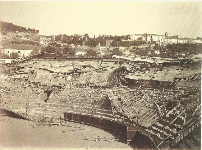 Plaza de toros destrozada. Así quedó la plaza de toros del Triunfo el 17 de agosto de 1889 tras el paso del ciclón. Todas las gradas del costado del lado Este las retorció y derrumbó hacia adentro. Al fondo se ve la muralla de la Cuesta Alhacaba y la zona del Carril de la Lona. Aparece la columna de la Virgen del Triunfo en su lugar primitivo, delante del cuartel de la Merced. 