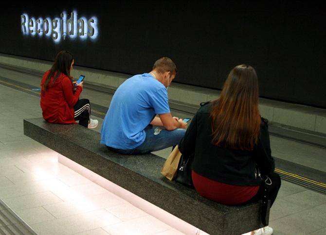 Jóvenes miran su móvil en la estación de Recogidas. 