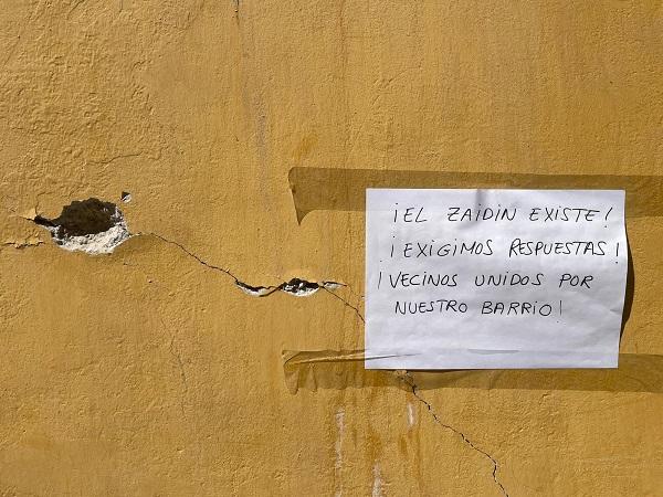 Cartel de protesta junto desperfectos en una fachada del Zaidín.