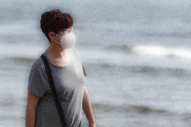 Una mujer con mascarilla pasea por una playa.