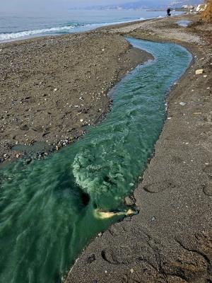 Agua azul verdosa vertida por la acequia al mar en la playa de La Cagaílla. 