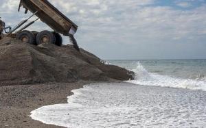 Un camión echa arena en Playa Granada mientras el agua se la lleva. 