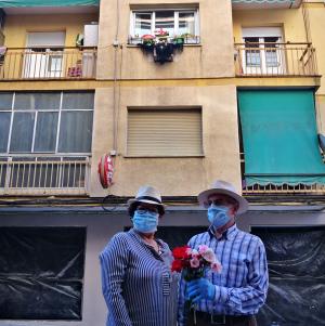 Una pareja, al regresar de su paseo, posa bajo la cruz que engalana su ventana.