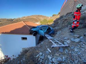 El coche, caído sobre la vivienda, apoyada en una ladera. 