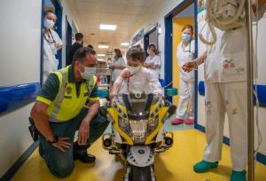 Un agente observa cómo disfruta un peque con la moto en un pasillo del hospital.